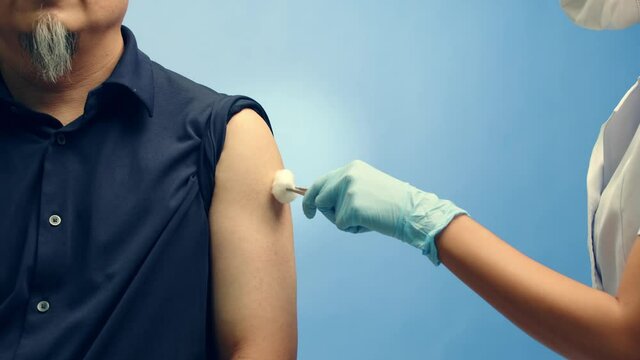 A nurse gives a vaccine injection in the arm of a patient - blue background