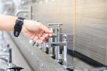 Male hand choosing stainless steel water tap in furniture store. Home improvement for domestic kitchen.
