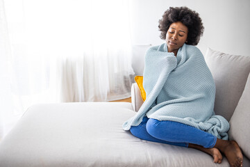 Sick young african woman feeling cold covered with blanket sit on sofa, ill black girl shivering...