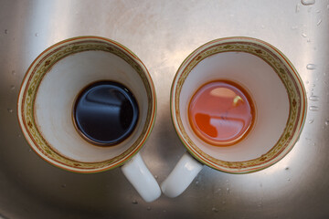 mug with leftover coffee and mug with leftover tea in the sink