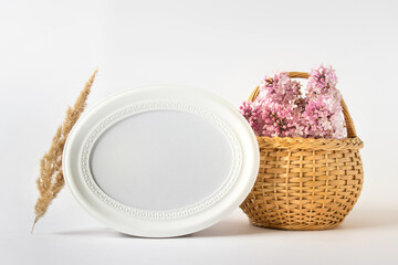 Mockup template with country style composition of round blank white frame, fluffy dry plant and wooden basket with lilac flowers.