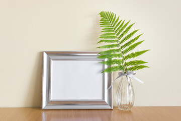 Mockup template with horizontal silver metallic wide frame and glass vase with forest wild fern leaf.