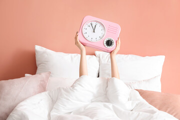 Young woman with clock in bedroom