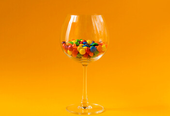 Colorful candies in a glass on yellow background