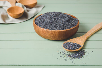 Bowl and spoon with poppy seeds on color wooden background
