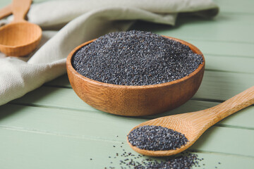 Bowl and spoon with poppy seeds on color wooden background