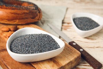 Bowls with poppy seeds on light wooden background