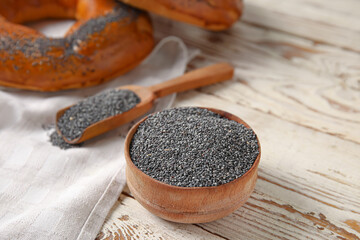 Bowl and scoop with poppy seeds on light wooden background