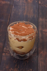 Tiramisu In A Glass Container Against A Dark Wood Countertop