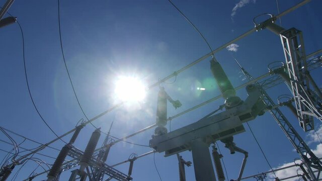 Glass insulators with cables on support at electricity distribution substation under blue sky at back sunlight close low angle shot