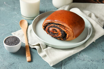 Tasty bun with poppy seeds and glass of milk on color background
