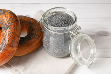 Jar with poppy seeds and tasty bagels on light wooden background