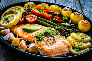 Roasted salmon steak with roast potatoes and vegetable salad served on black plate on wooden table
