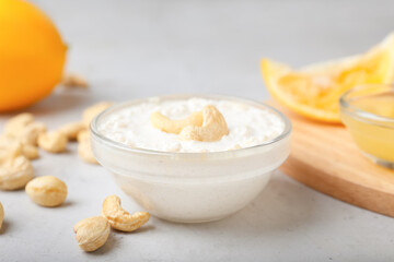 Bowl with cashew sour cream, nuts and lemon juice on light background, closeup