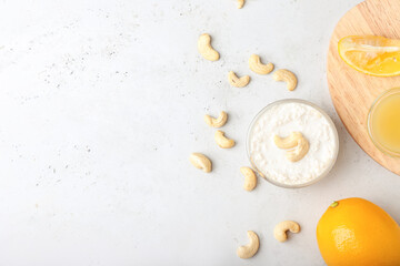 Bowl with cashew sour cream, nuts and lemon juice on light background