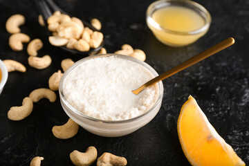 Bowl with cashew sour cream, nuts and lemon juice on dark background, closeup