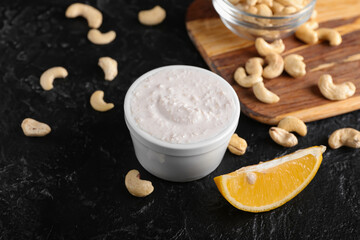 Bowl with cashew sour cream, slice of lemon and nuts on dark background