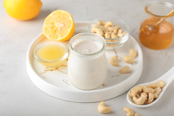 Tray with cashew sour cream, nuts, honey and lemon juice on light background