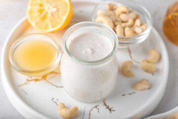 Tray with cashew sour cream, nuts and lemon juice on light background, closeup