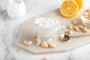 Gravy boat with cashew sour cream, nuts and lemon on light background