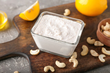 Bowl with cashew sour cream, lemon and nuts on grey background, closeup