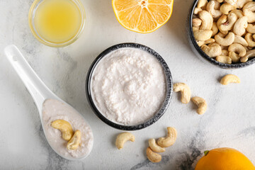 Bowls with cashew sour cream, nuts and lemon juice on light background