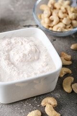 Bowl with cashew sour cream and nuts on grey background, closeup
