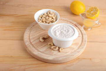 Bowls with cashew sour cream, nuts and lemon juice on wooden background