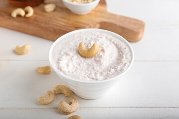 Bowl with cashew sour cream and nuts on light wooden background, closeup