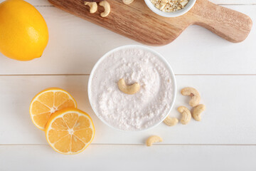 Bowl with cashew sour cream, nuts and lemon on light wooden background