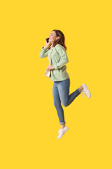 Jumping young woman talking by mobile phone on color background