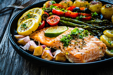 Roasted salmon steak with roast potatoes and vegetable salad served on black plate on wooden table
