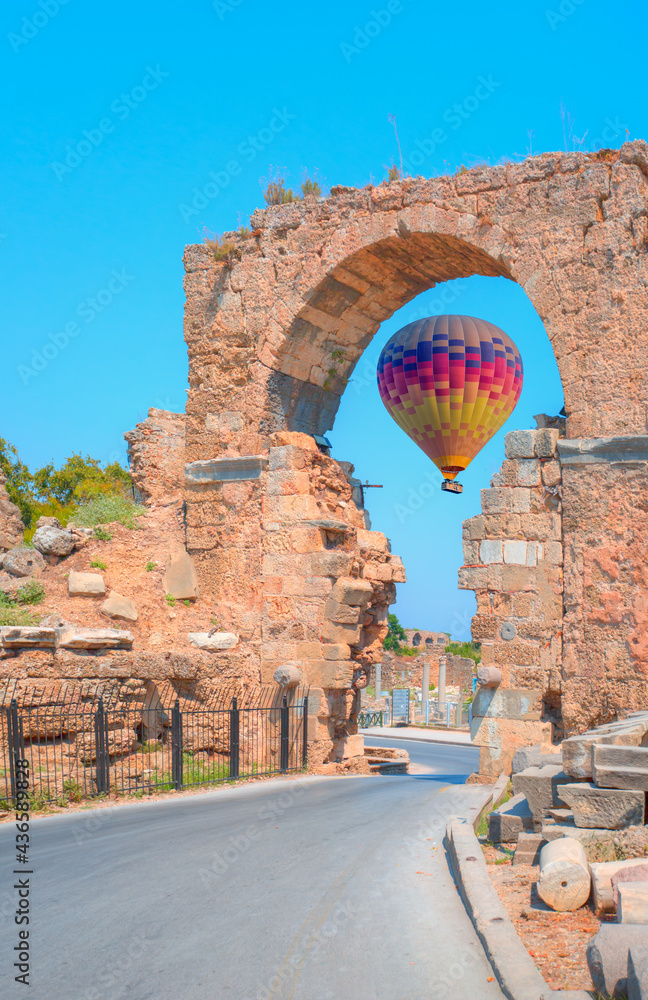 Wall mural Ruins of ancient city in Side - Hot air balloon flying over old gates to antique theater - Antalya, Turkey