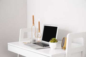 Modern workplace with laptop and candlestick near light wall