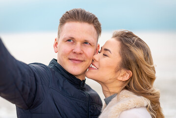Fototapeta premium Beautiful young happy woman hugging cuddle young boyfriend while taking selfie photo on sunny beach.Close up.