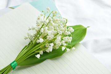 Beautiful lily-of-the-valley flowers and notebook on light background, closeup