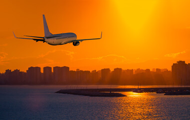 Passenger airplane flying over the city at sunset