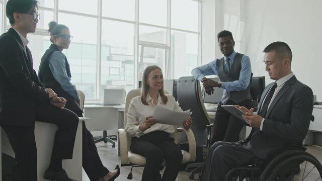 Medium shot of diverse team of colleagues in formal wear having casual meeting in office