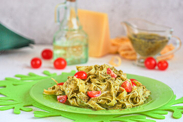 Fettuccine pasta with pesto, pine nuts, cherry tomatoes and grated Parmesan on a green plate. Italian cuisine. Home cooking.