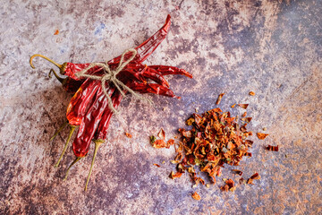 Pile of crushed red pepper, Cayenne pepper, dried chilli on a motley background. Next to a bunch of whole dry chili peppers. It is a popular spicy condiment for Mexican dishes.