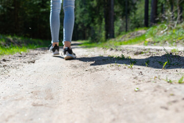 Rear view photo of female tourist legs walking in a forest road.Summer day.Selective focus.