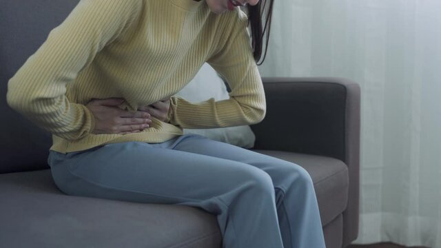 Asian women with menstruation and menstrual cramps. a girl sitting in pain on sofa. woman had severe abdominal pain caused by gastritis. concept Stomachache.