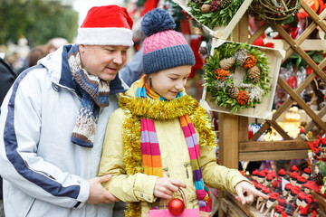 Young father with daughter having fun on Christmas fair, selecting decoration for home..