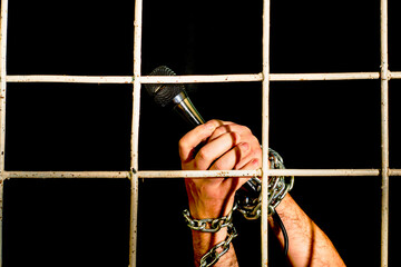 the concept of human rights freedom of speech hands shackled with an iron chain hold a microphone behind an iron prison bars