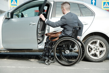 Businessman in wheelchair opening door of his car in urban environment