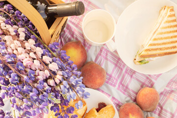 Picnic in nature. Basket with flowers, wine, peaches, sandwiches on the tablecloth on a Sunny day, top view