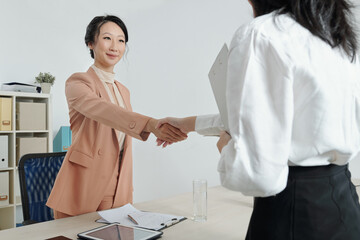 Positive young businesswomen shaking hands after discussing important issues at meeting