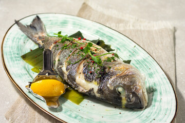 Sea carp cooked with white wine, served with a lemon wedge and garnished with young herbs. Summer menu concept.