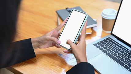 Close up businesswoman using mobile phone and working with laptop at office desk.