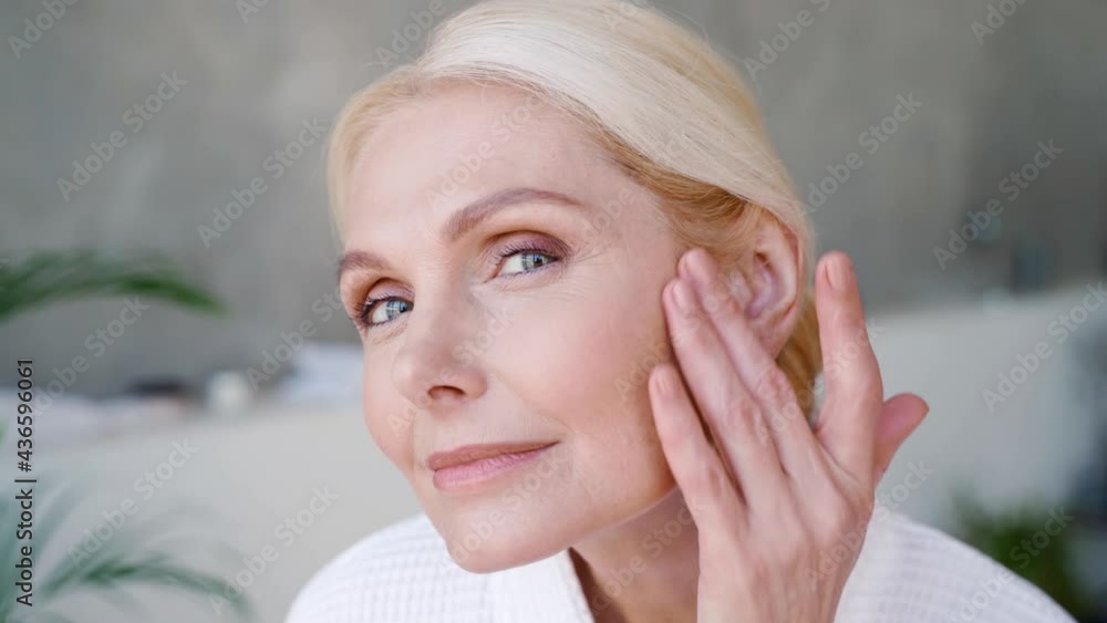 Poster portrait of happy smiling attractive middle aged woman wearing bathrobe touching perfect skin lookin